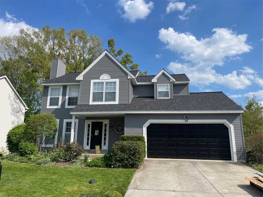 A gray house featuring a garage and a driveway, set against a clear sky.
