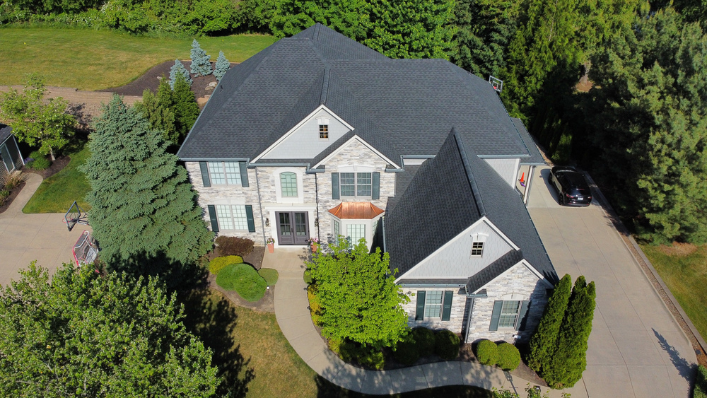 Aerial perspective of a sizable house with a prominent driveway and green surroundings.