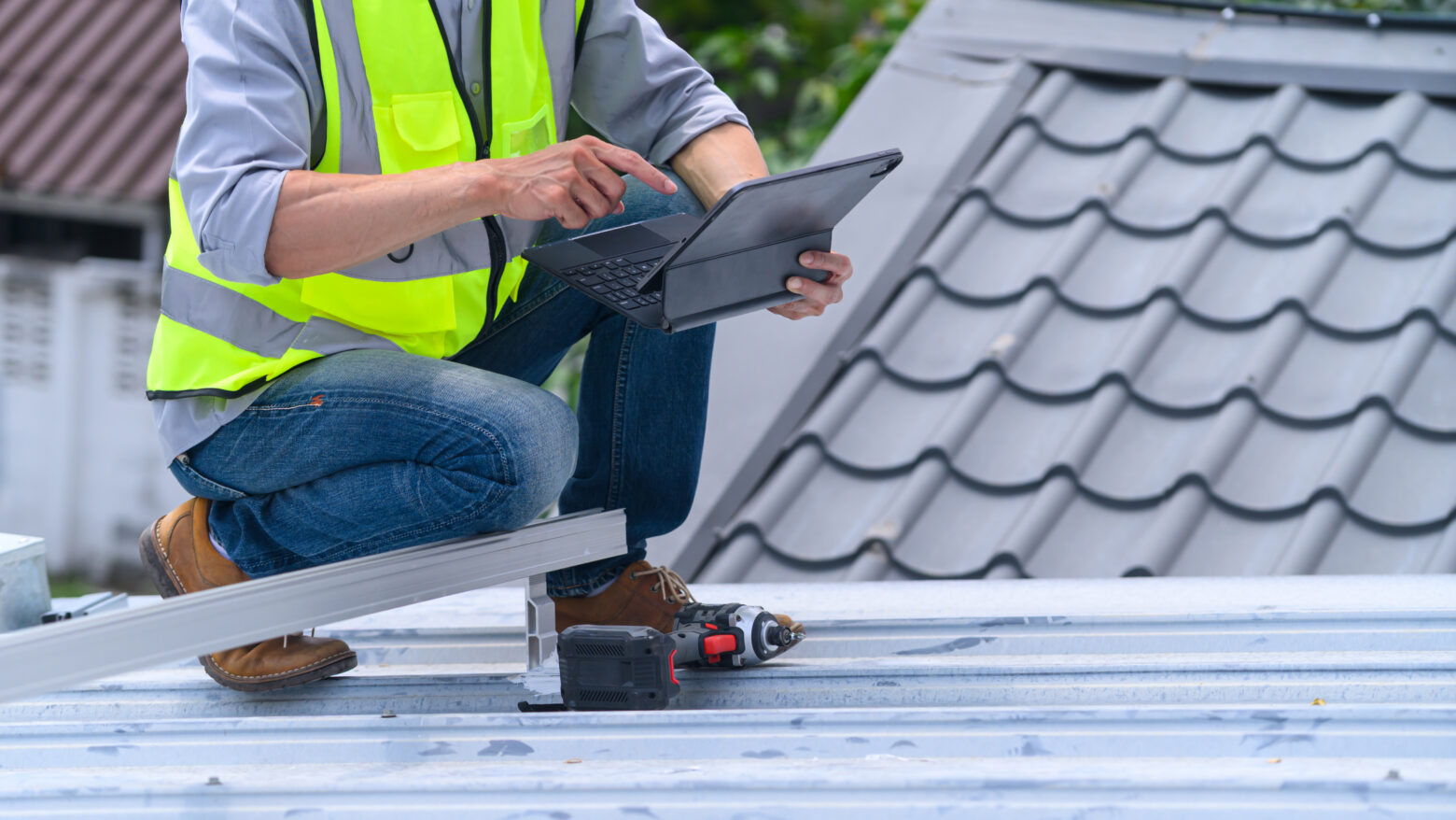 Roofer in Safety Vest Using Tablet on Metal Roof During Construction Inspection